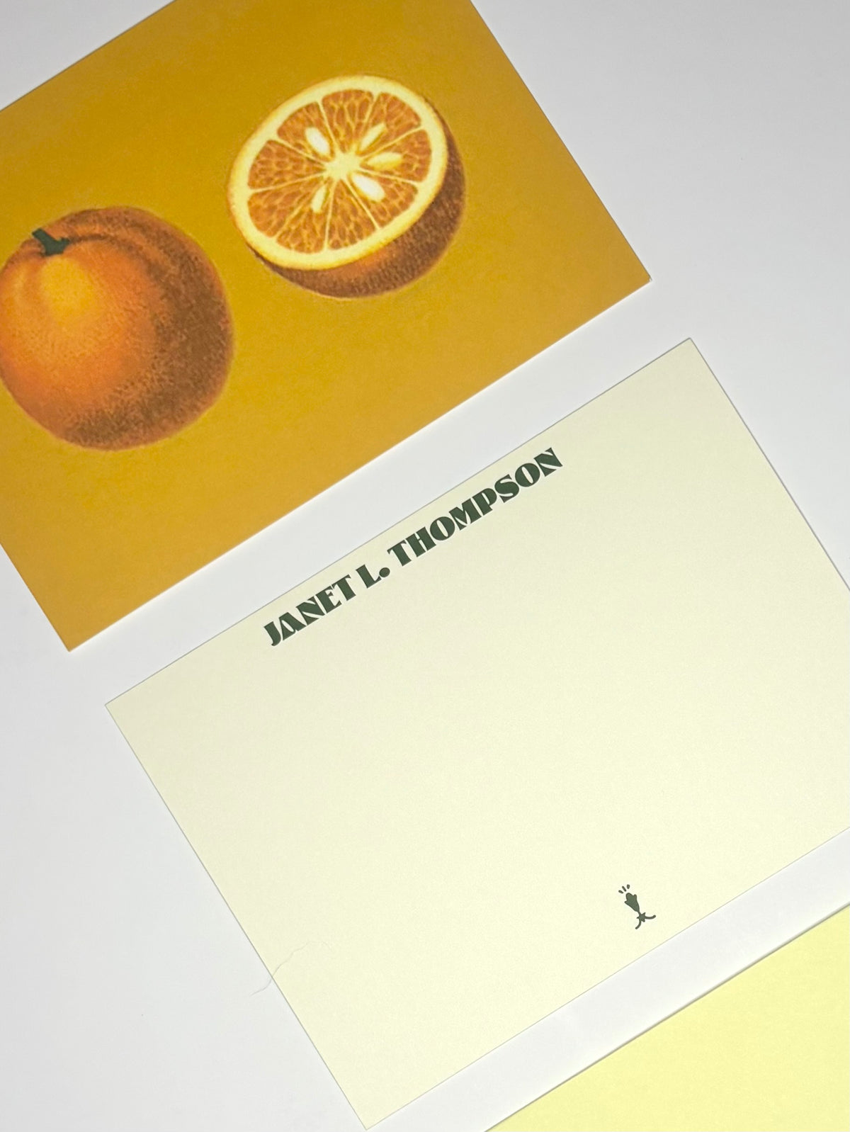 Close-up of Golden Orange stationery showing whole and halved oranges on gold and a personalized cream writing side.