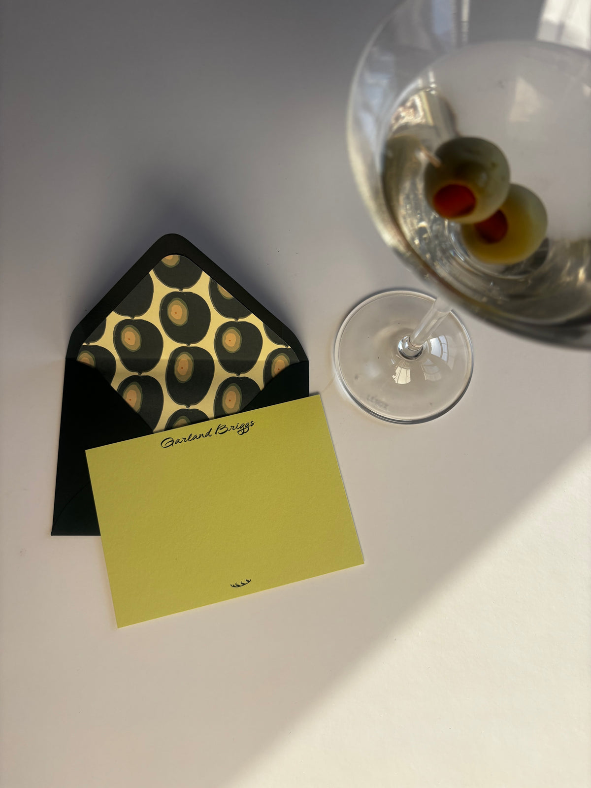 Martini Olive notecard and olive-lined envelope beside a martini glass with two olives.